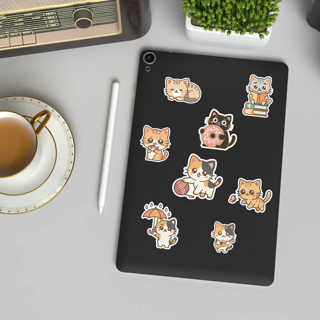 Black tablet with cat-themed stickers on a desk with a cup of tea and pen.